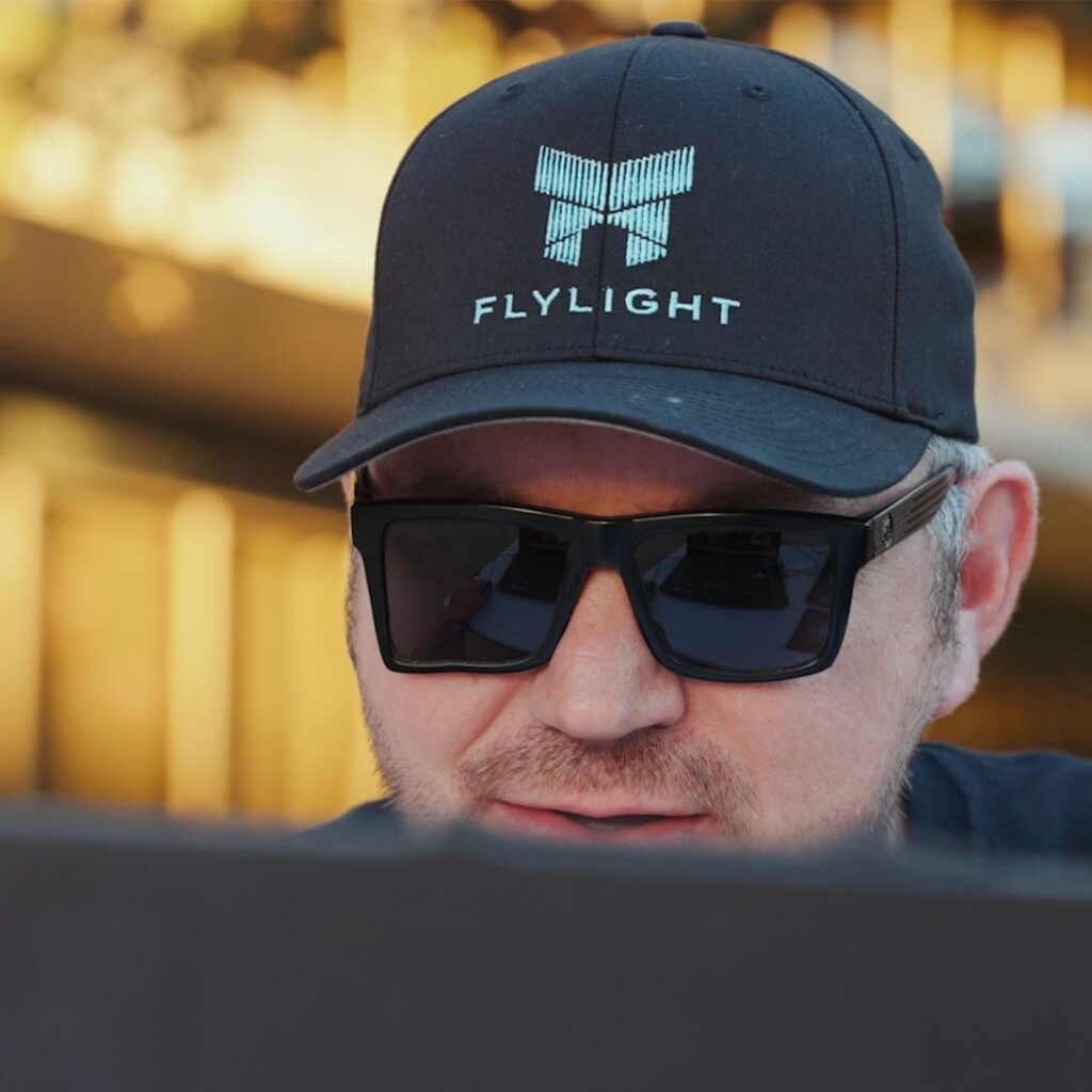 Man in sunglasses and Flylight cap using laptop