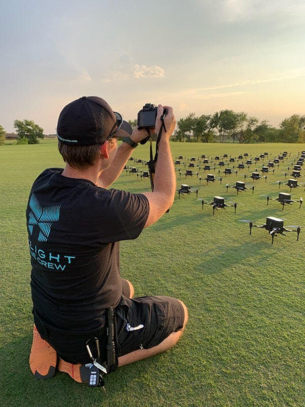 Man photographing drones on field at sunset