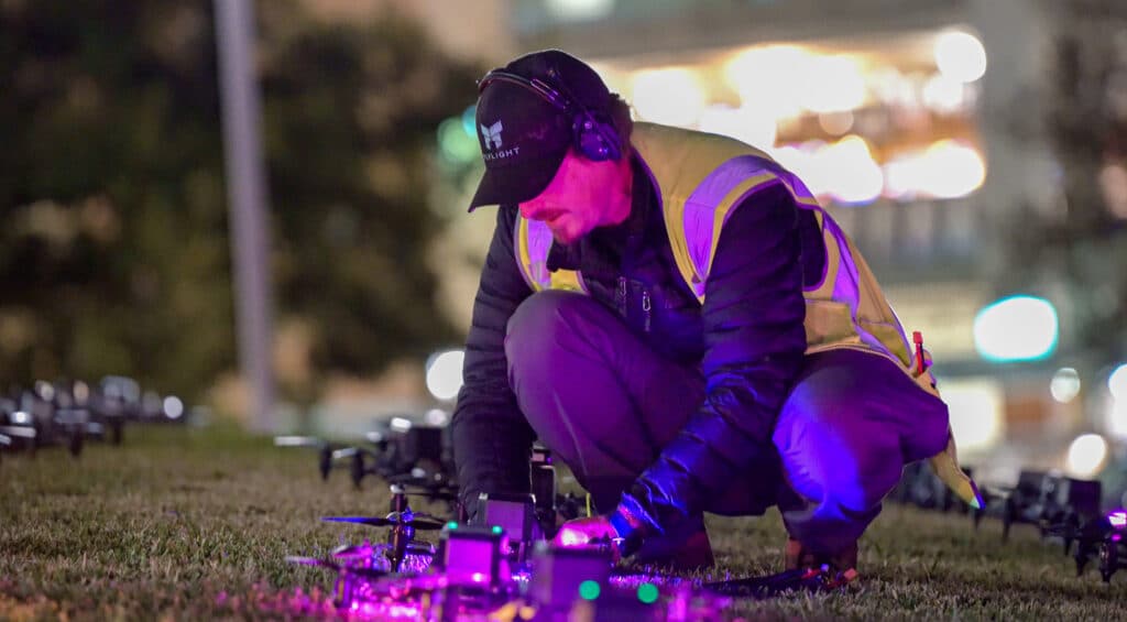 Man adjusting drone at night with illuminated city background