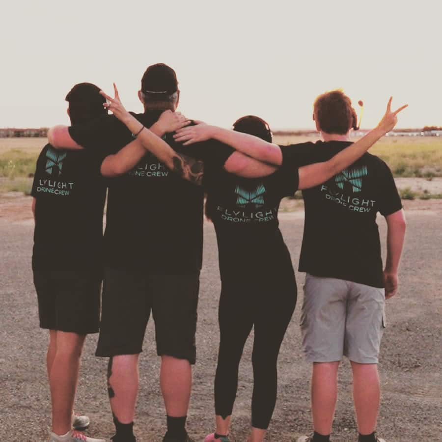 Friends with arms over shoulders wearing matching shirts at sunset