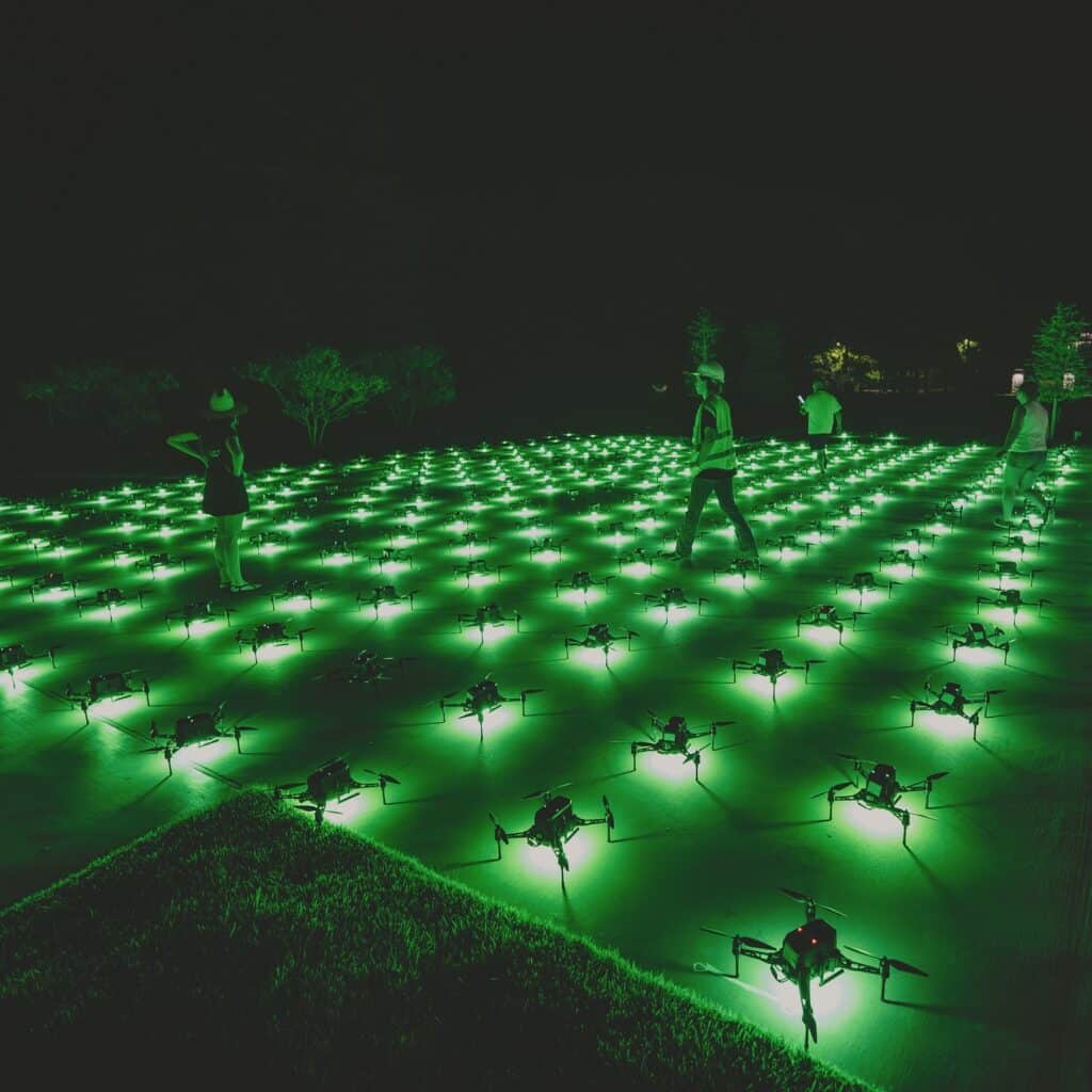 People exploring green lit drone light installation at night